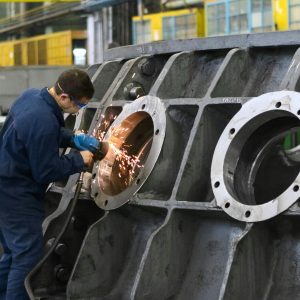 A worker in protective gear grinding metal, creating sparks in a factory setting.